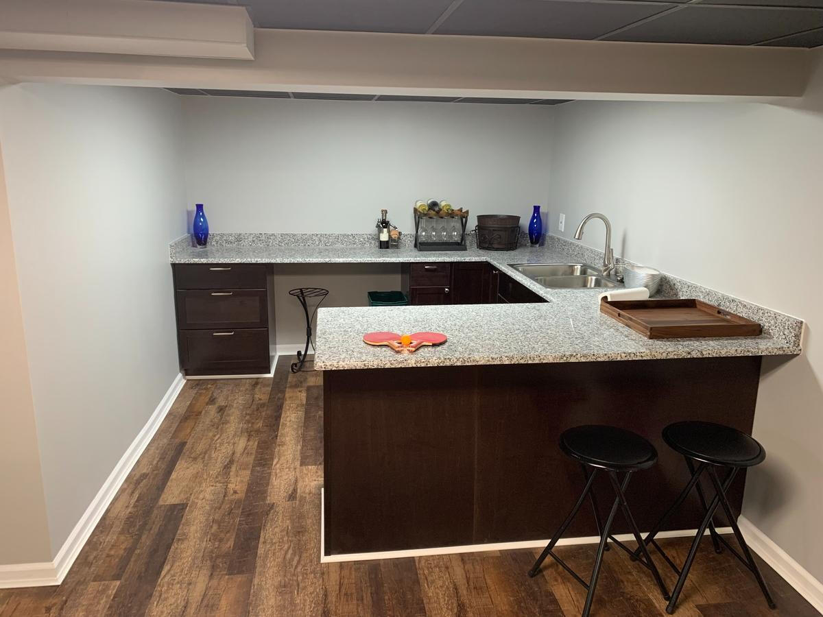 Custom Basement Bar Renovation – Troy, MI Finished basement with L-shaped granite bar, modern cabinetry, and dark hardwood-style flooring – entertainment-focused remodel in Troy, Michigan