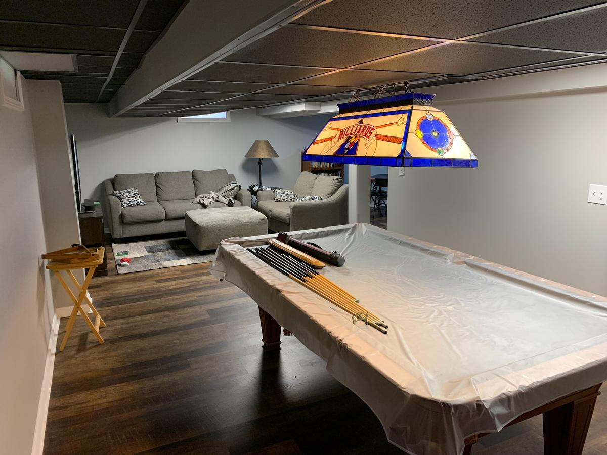 Entertainment-Focused Basement Remodel – Ferndale, MI Fully finished basement designed for recreation with a pool table, sectional sofa, and wood-look flooring – completed remodel in Ferndale, Michigan