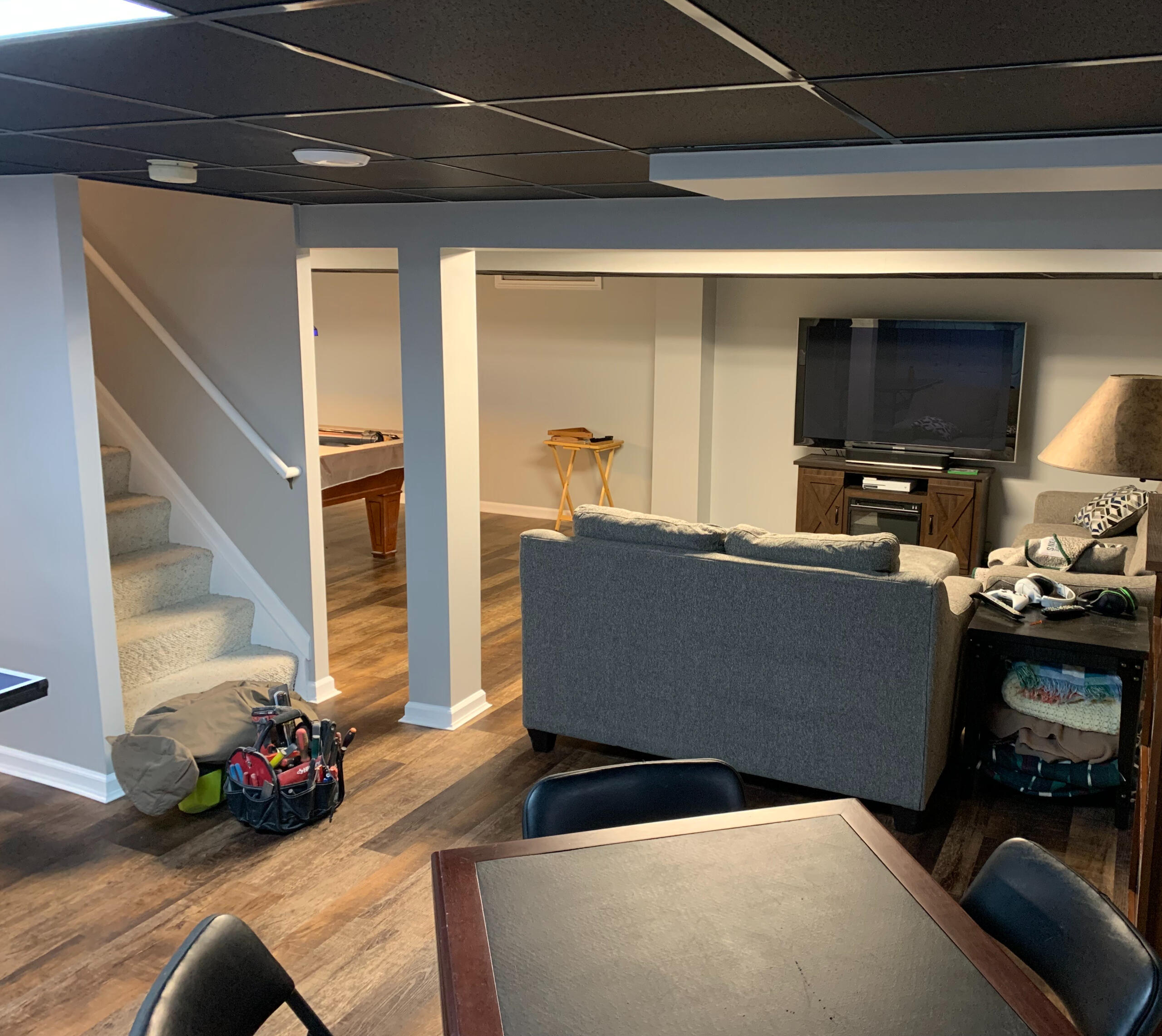 Finished Basement Remodel with Game Area – Royal Oak, MI Modern basement remodel featuring dark ceiling tiles, LVP flooring, and a multi-zone layout with a game table and entertainment seating – completed in Royal Oak, Michigan